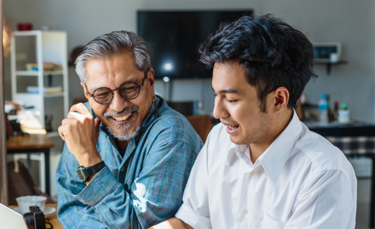 father and son sitting at computer and smiling